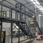 linia granulowania , zdjecie przedstawia układ zaspiracji pary i pyłów składającą się z rur, cyklonów i wentylatorów. silos na pellet oraz podajnik taśmowy do transportu pelletu